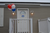 A photo of the front door of a double-wide manufactured home and multicolored balloons.